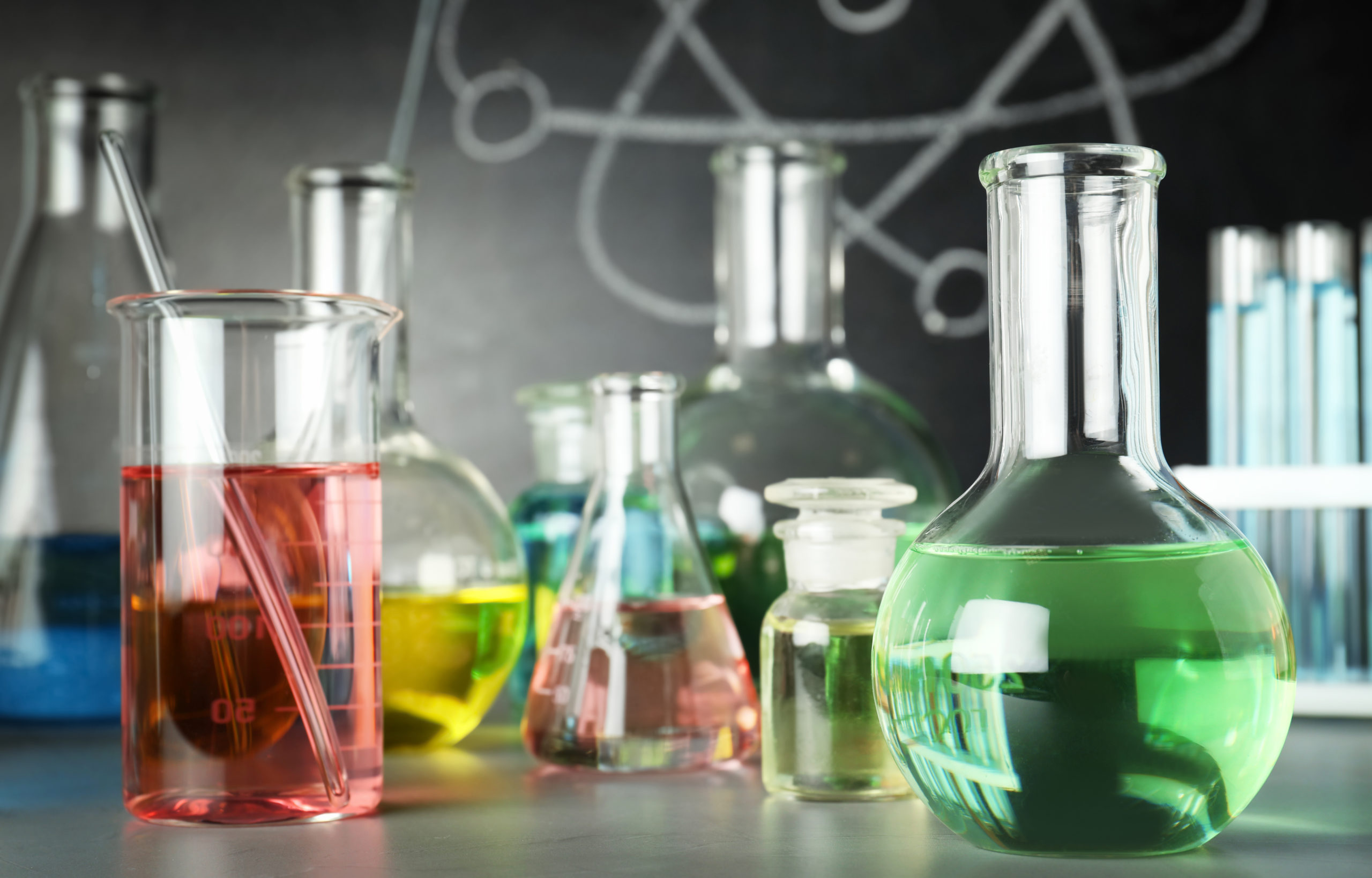 Laboratory glassware on table near chalkboard. Chemistry concept